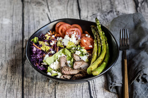 Bowl of salad with steak, asparagus, tomatoes, shredded red cabbage, lettuce and feta cheese - SBDF04606