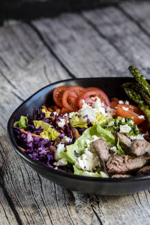 Bowl of salad with steak, asparagus, tomatoes, shredded red cabbage, lettuce and feta cheese - SBDF04607