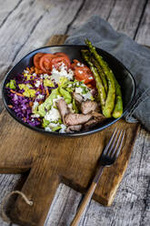 Bowl of salad with steak, asparagus, tomatoes, shredded red cabbage, lettuce and feta cheese - SBDF04608
