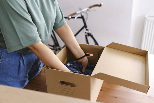 Junge Frau packt Kleidung in Karton - ASGF03459