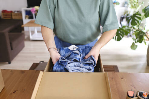 Junge Frau verpackt Jeans in einem Karton zu Hause - ASGF03460