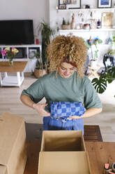 Young woman packing order in cardboard box at home - ASGF03467