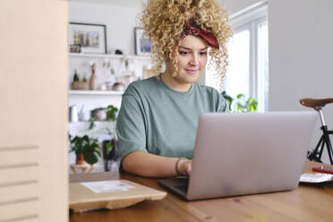 Smiling businesswoman working on laptop at desk - ASGF03479