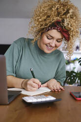 Smiling businesswoman writing on note pad at desk - ASGF03481
