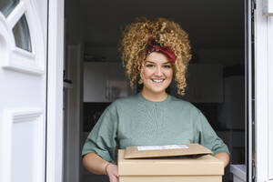 Glückliche junge Frau mit Paketen vor der Tür stehend - ASGF03490