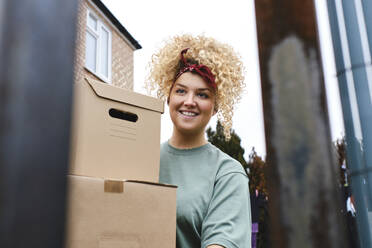 Lächelnde junge Frau mit lockigem Haar, die Pakete ausliefert - ASGF03499
