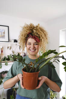 Lächelnde Frau steht mit Topfpflanze zu Hause - ASGF03505