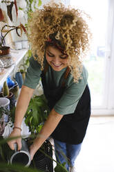 Lächelnde Frau beim Gießen von Pflanzen zu Hause - ASGF03506