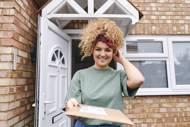 Glückliche Frau steht mit Paket vor einem Haus - ASGF03518