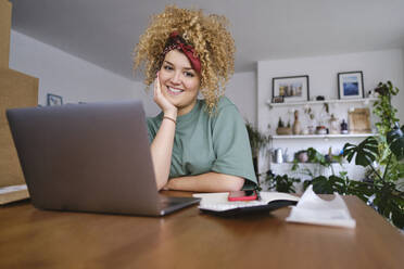 Smiling young businesswoman sitting at desk with laptop - ASGF03520