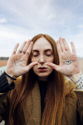 Frau mit geschlossenen Augen zeigt Tätowierung auf Handfläche - MEUF09027