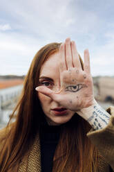 Frau zeigt Augen-Tätowierung auf der Hand auf der Terrasse - MEUF09028