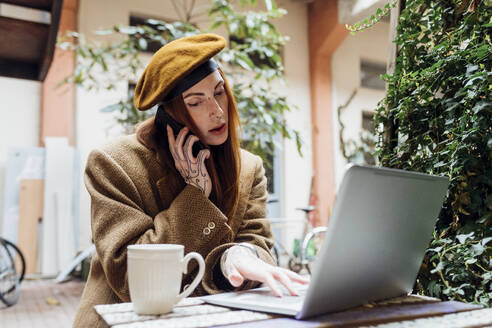 Frau telefoniert und benutzt Laptop in einem Straßencafé - MEUF09031