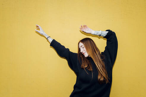 Carefree woman with arms raised enjoying in front of yellow wall - MEUF09044