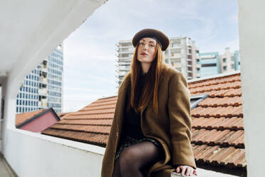 Confident woman wearing beret hat sitting on wall - MEUF09075