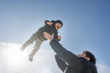 Playful father throwing son in air on sunny day - ANAF01142