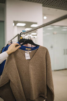Besitzerin hängt Kleidung auf einem Regal im Laden auf - ANAF01151
