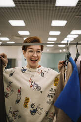 Happy woman standing by clothing rack - ANAF01153
