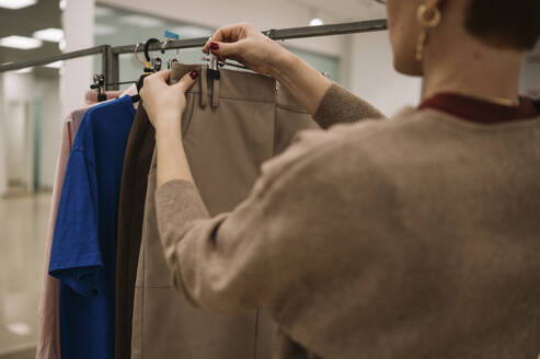 Ladenbesitzer hängt Kleidung auf einem Regal im Laden auf - ANAF01158