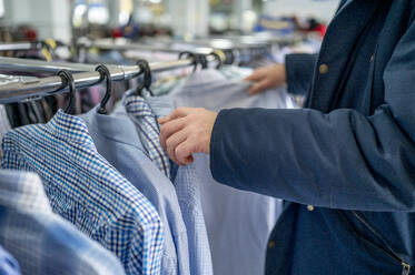 Mann wählt Kleidung von einem Regal im Geschäft aus - ANAF01165