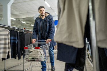 Mann mit Einkaufswagen sieht sich Kleidung an - ANAF01168