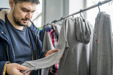 Mann untersucht grauen Kapuzenpulli in Bekleidungsgeschäft - ANAF01170