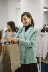 Glückliche Geschäftsfrau beim Verteilen von Einkaufstaschen im Geschäft - ANAF01182