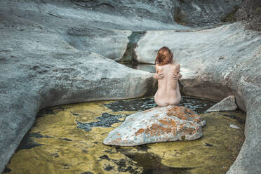 Nackte junge Frau sitzt auf einem Felsen in einem schmutzigen Fluss - PCLF00341