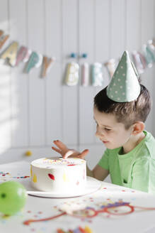 Boy touching birthday cake on table at home - ONAF00457