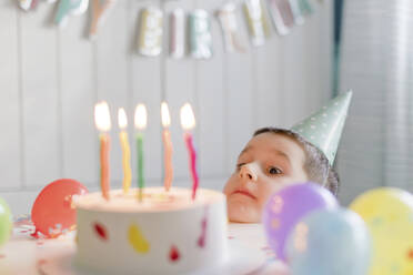 Playful boy looking at birthday cake with candles - ONAF00460