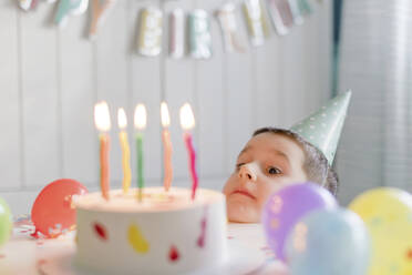 Verspielter Junge schaut auf Geburtstagskuchen mit Kerzen - ONAF00460