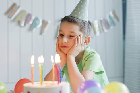 Sad elementary boy looking at birthday cake - ONAF00461