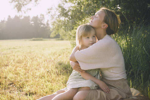 Mutter umarmt Tochter in der Natur sitzend - NDEF00428