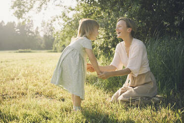 Happy mother holding hands with daughter on sunny day in nature - NDEF00429