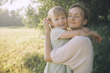 Smiling mother hugging daughter on sunny day in nature - NDEF00430