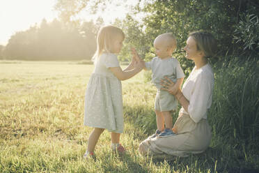 Glückliche Mutter mit Sohn und Tochter spielen zusammen in der Natur an einem sonnigen Tag - NDEF00431