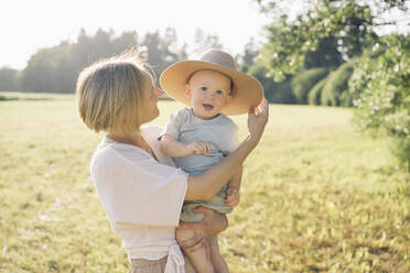 Glückliche Mutter mit Sohn mit Hut in der Natur an einem sonnigen Tag - NDEF00440