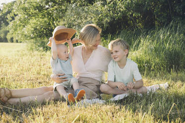Happy mother sitting with sons in nature - NDEF00443
