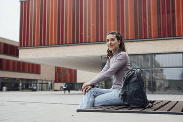 Lächelnde Frau mit Rucksack vor einem Gebäude sitzend - JOSEF18188