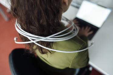 Businesswoman using laptop trapped in cable at office - JOSEF18205