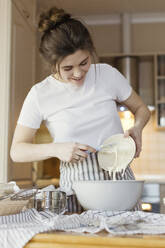 Happy woman pouring sourdough in bowl - ONAF00466