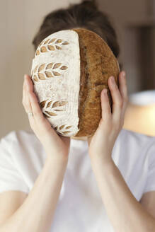 Junge Frau bedeckt ihr Gesicht mit einem Laib Brot zu Hause - ONAF00482