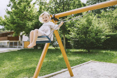 Happy girl swinging on swing at park - NDEF00456