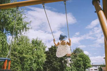 Girl wearing hat swinging on swing at park - NDEF00460