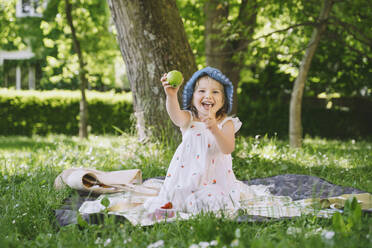 Happy girl gesturing and showing green apple in garden - NDEF00461