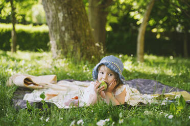 Mädchen isst grünen Apfel auf Gras im Garten liegend - NDEF00462