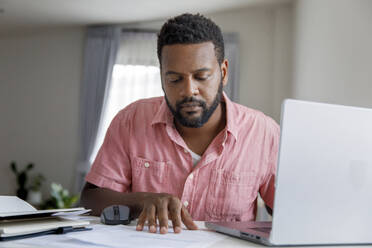 Freelancer examining and reading document at desk - IKF00006