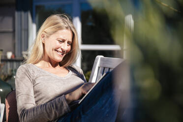 Lächelnder Freiberufler mit Tablet-PC im Vorgarten sitzend an einem sonnigen Tag - JOSEF18233