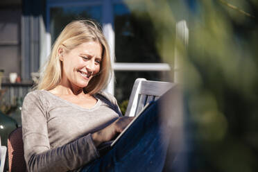 Smiling freelancer using tablet PC sitting at front yard on sunny day - JOSEF18233