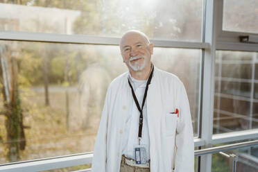 Porträt eines lächelnden Oberarztes, der sich am Geländer eines Krankenhauskorridors anlehnt - MASF36161